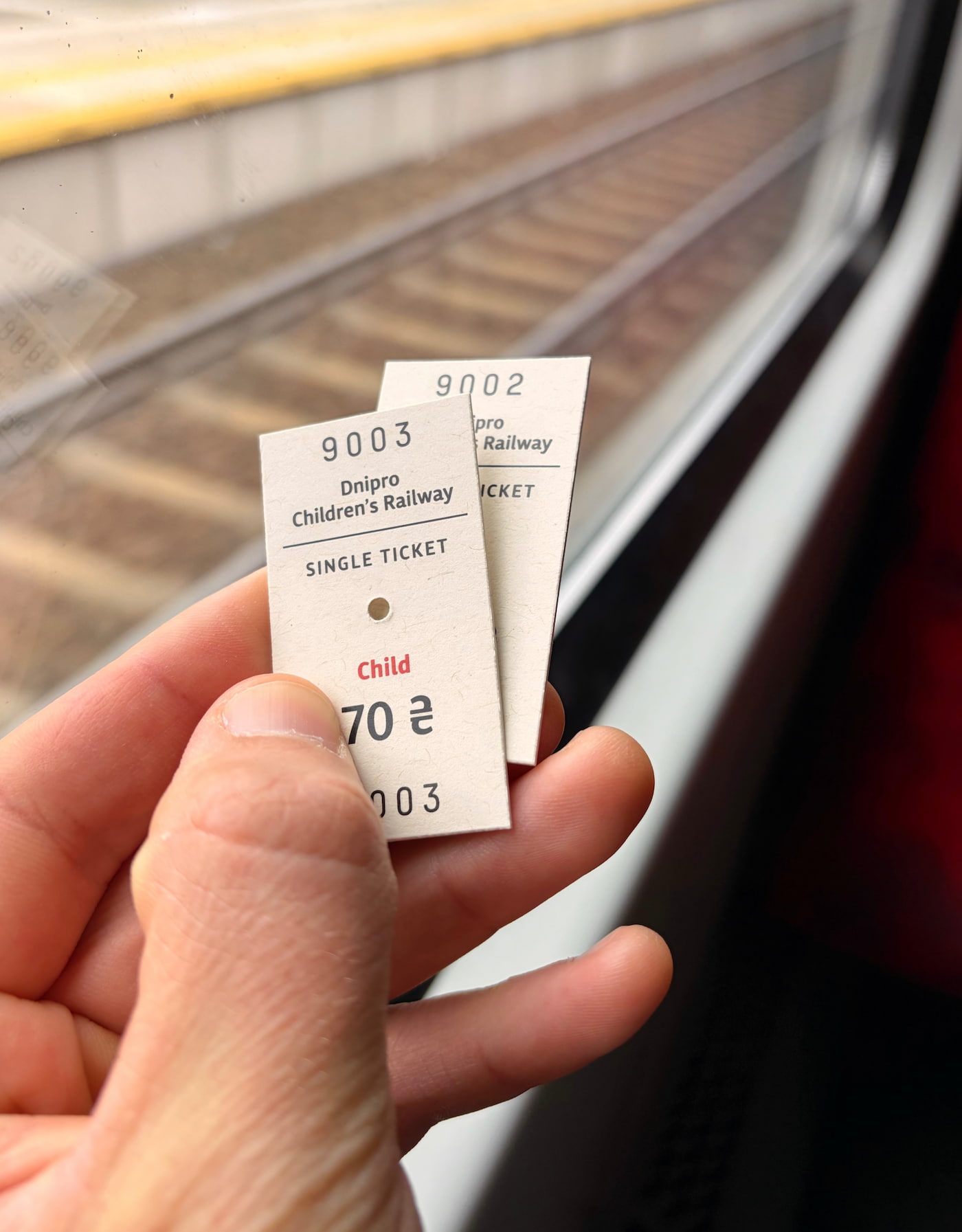 Two tickets for the Dnipro Children’s Railway held in hand by a train window